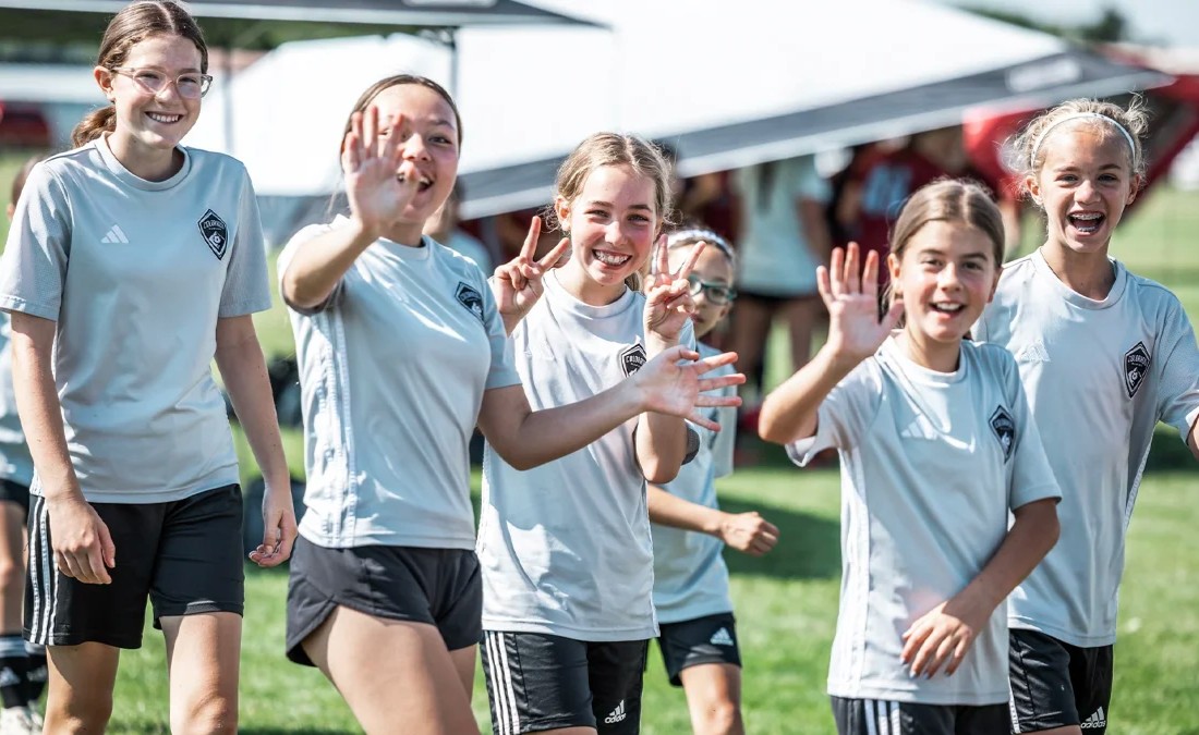 A group of smiling young girls on a recreational soccer team wave at the camera during a Storm event
