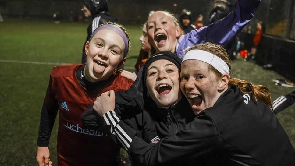 A group of young girls celebrate together in the rain during a Storm international soccer trip