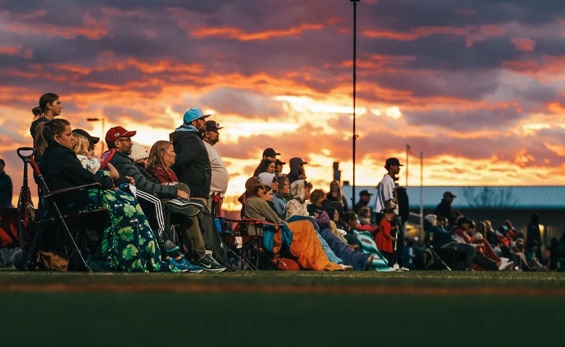 Parents and fans watching a youth soccer game during a sunset in Colorado
