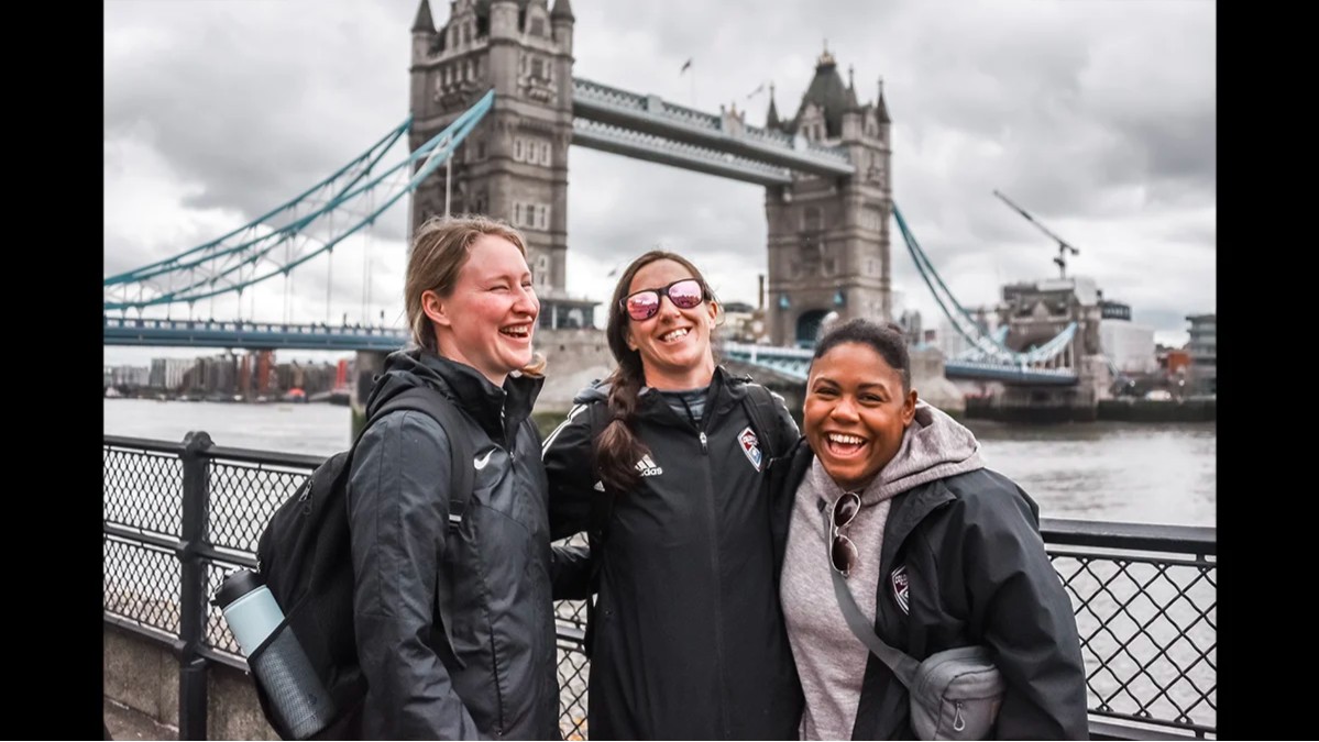 Three Storm soccer coaches laugh together in front of Tower Bridge during an international trip to London