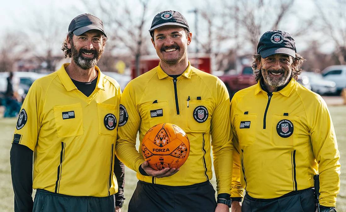 Three certified soccer referees in yellow uniforms holding a match ball in Colorado