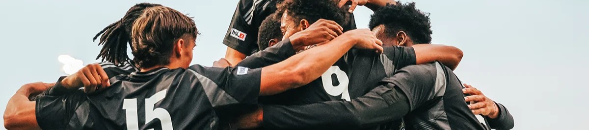 USL2 soccer players celebrating a goal with a team huddle during a Storm match in Denver