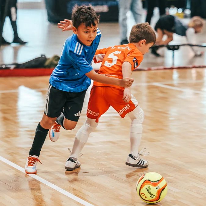 Young boy in a blue futsal uniform dribbling past an orange defender in Colorado