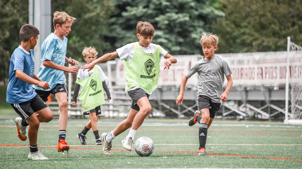 Young boys competing for the ball during a soccer scrimmage at a Storm summer camp