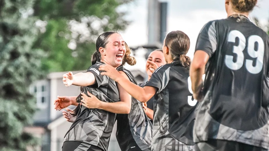 Young female soccer players in black jerseys laughing and hugging after scoring a goal in Denver 2