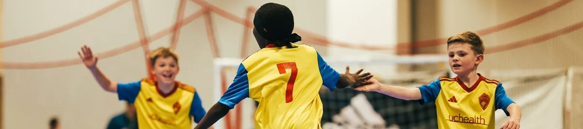 Youth futsal players in yellow and blue uniforms high fiving on an indoor court in Colorado 1