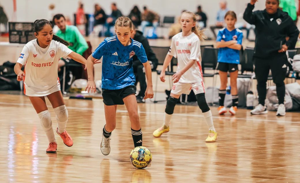 Youth girl in a blue futsal jersey dribbling a ball during an indoor Colorado match 2