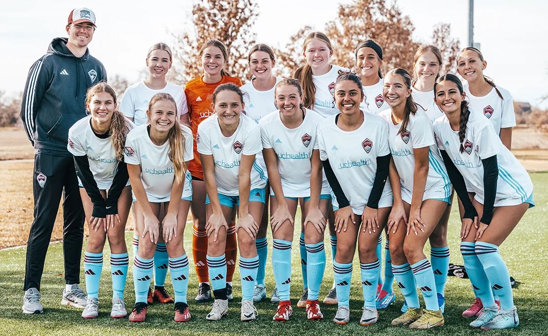Youth girls soccer team smiling with their coach on the field after a game in Colorado