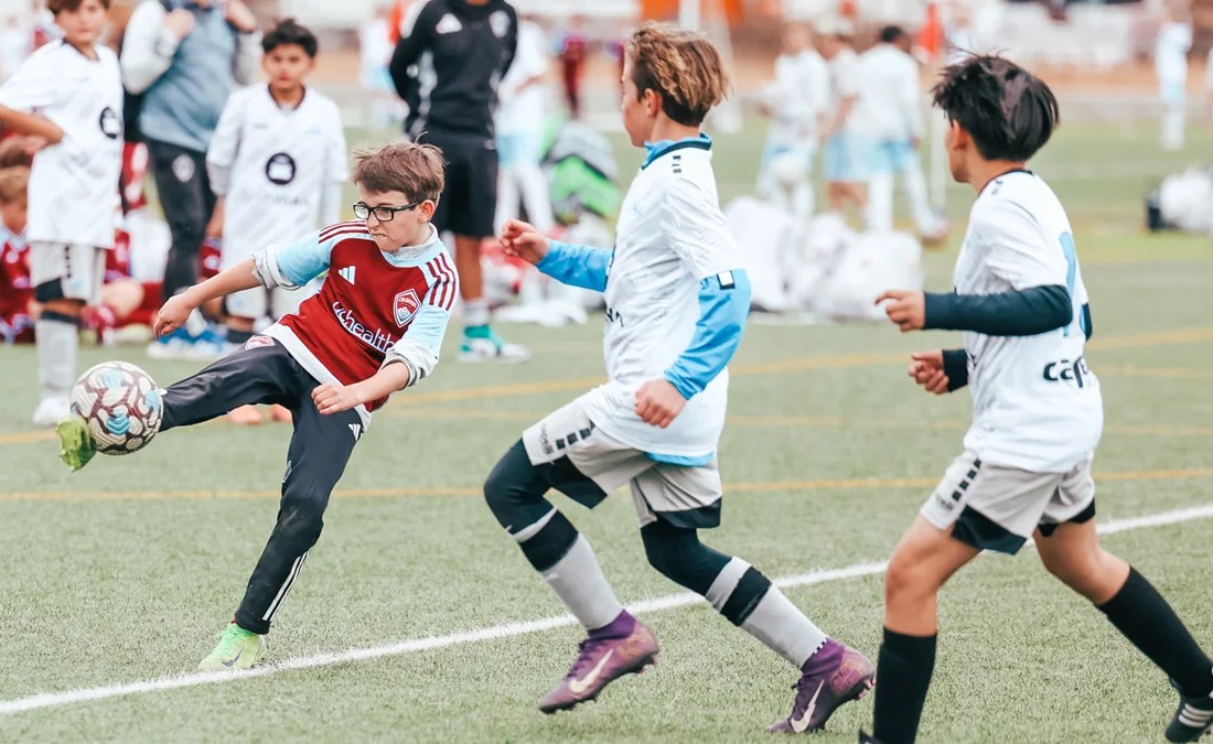 young soccer player in a maroon jersey kicking the ball during a competitive match in colorado